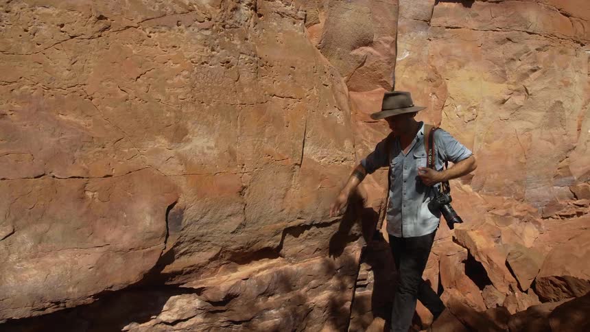 A photographer walks along a rock face on a hot and sunny day