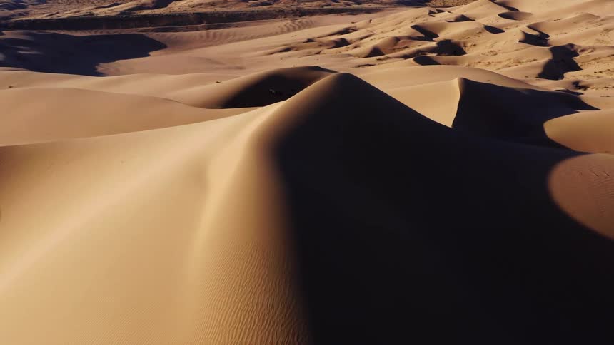 Aerial view of tall sand dunes in the desert near the mountains