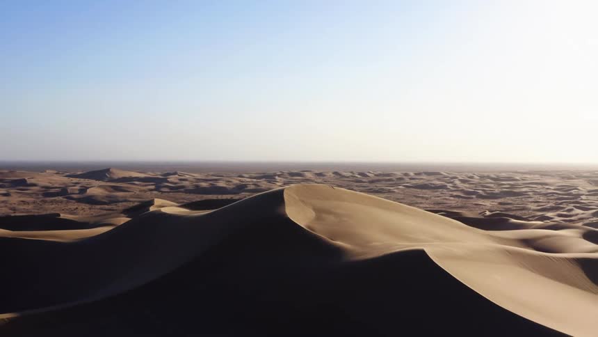 A desert with sandy dunes with the sky and clouds in the background
