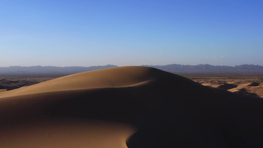 Aerial view of tall sand dunes in the desert near the mountains
