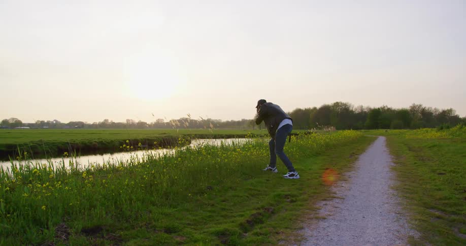 Man stands on the grass and leans towards a stream