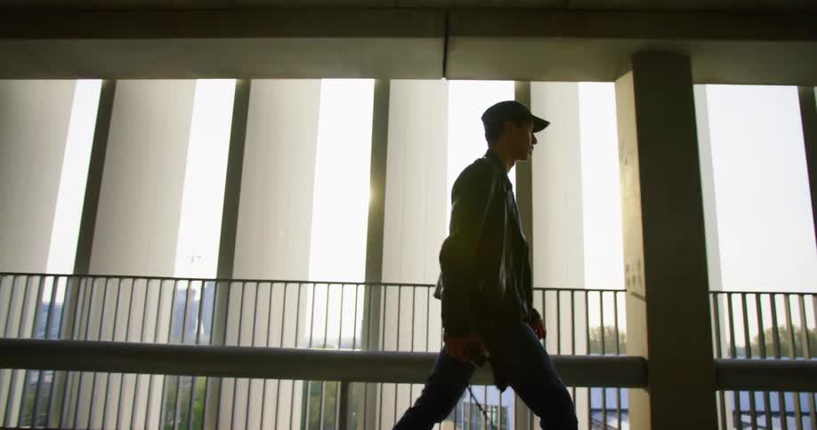 A man with a jacket and a hat walking in a building with the sky in the background