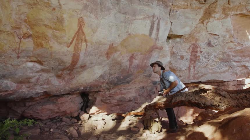 A photographer takes a photograph of primitive paintings on a rock face