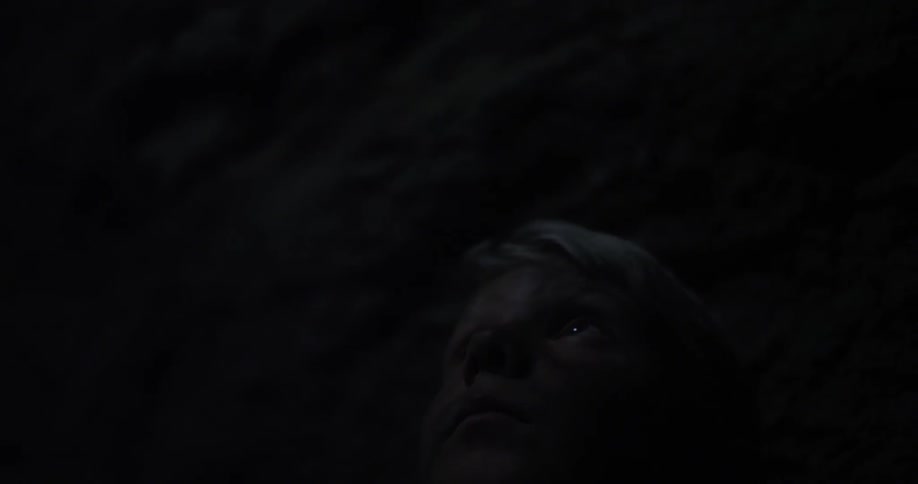 A boy with a dirty face looks up as he sits in a dark cave
