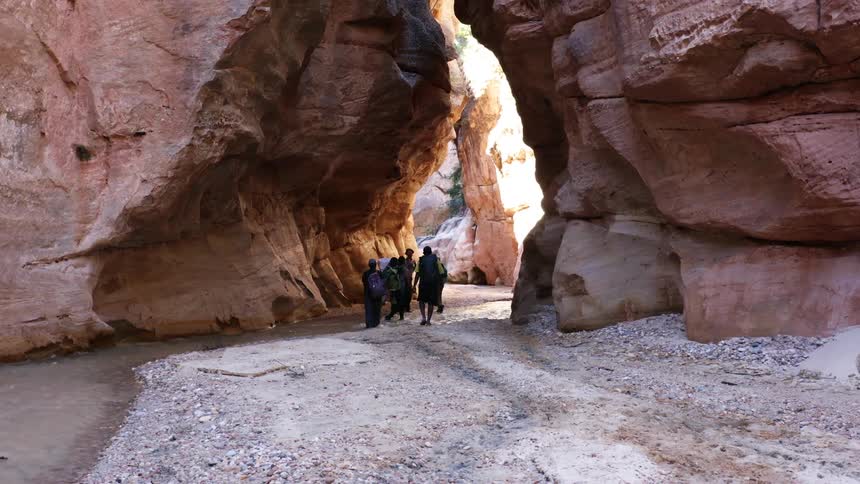 Group of people walk in a stream running between large rocks