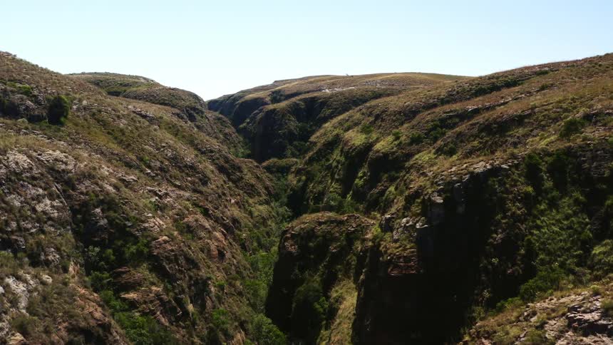 A canyon with grass and plants with the sky and clouds in the background
