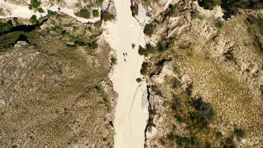 Three people walk together through a sandy ravine