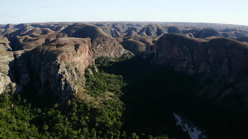 A canyon with trees and hills with the sky and clouds in the background