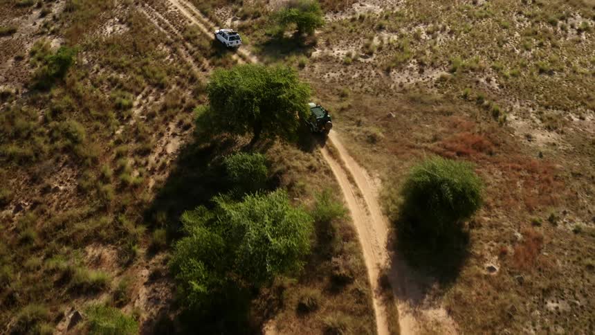 Two vehicles travel on a dirt road running through a field