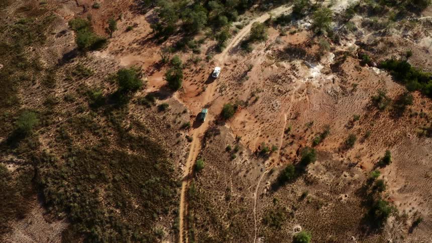 Two vehicles drive across the land towards a forest