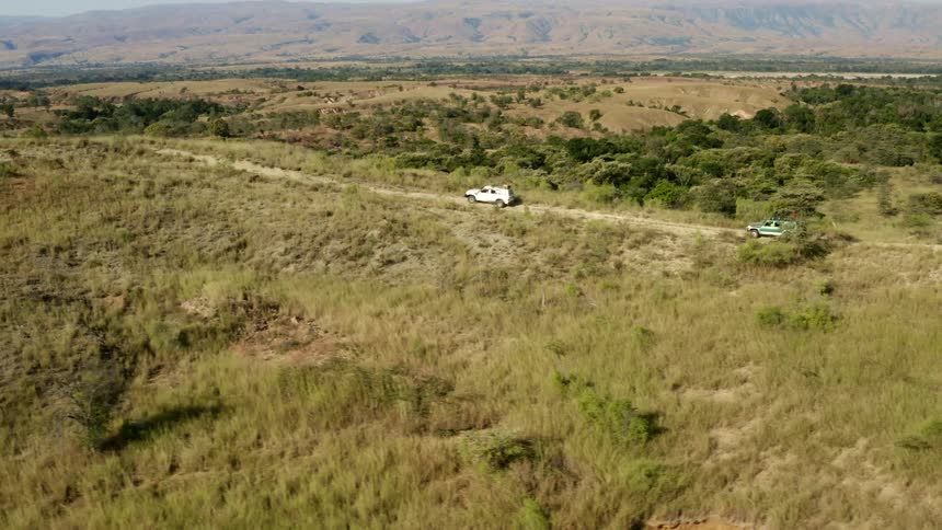 A pair of vehicles travel along a dirt road on a hill overlooking a vast grassland