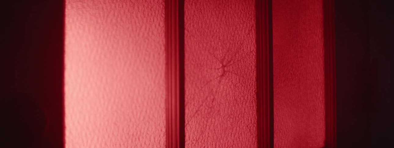 A red mist floats behind a broken glass window in the dark