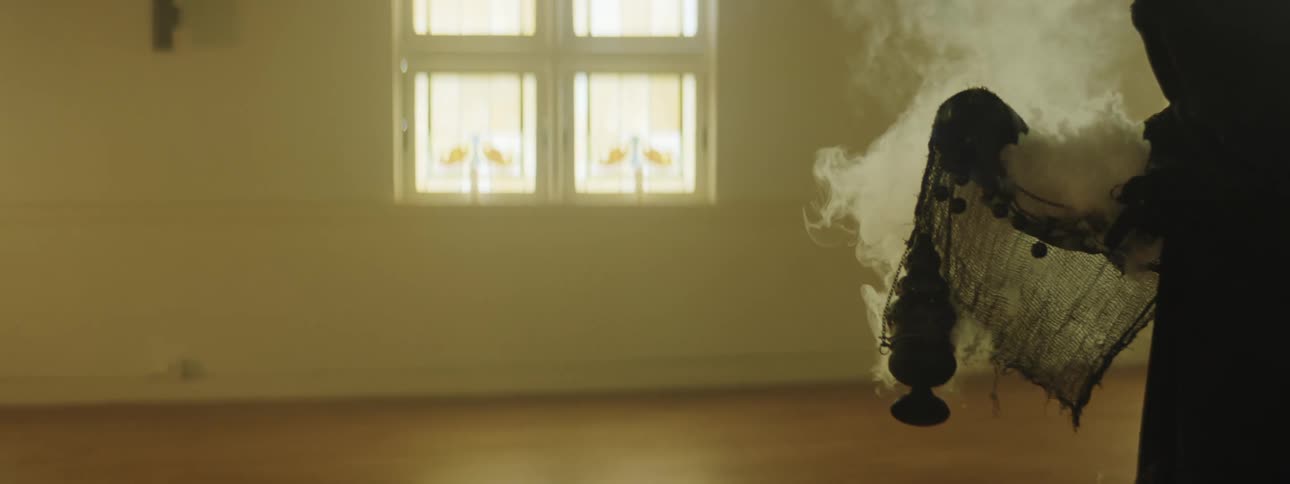 Monk wearing full body robe spreads incense smoke with a thurible inside a church