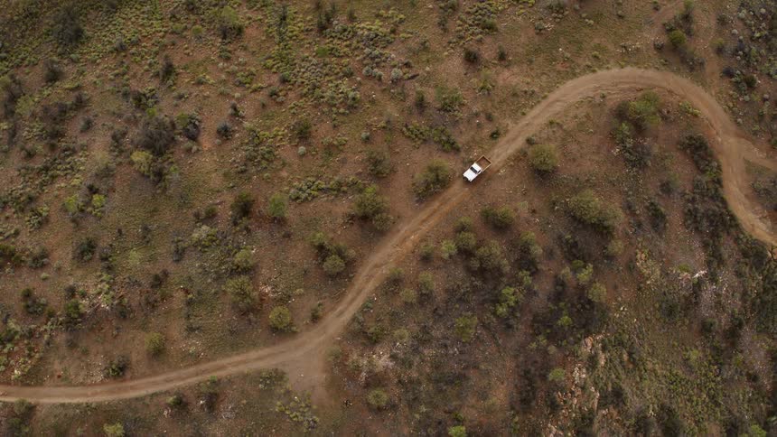 Aerial view of a white pickup truck driving on a winding dirt road
