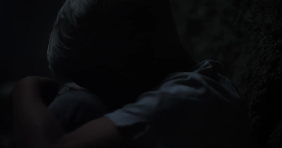 A child is crouched down in a dark area