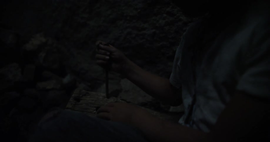 A person stabs a piece of wood with a large nail in the dark