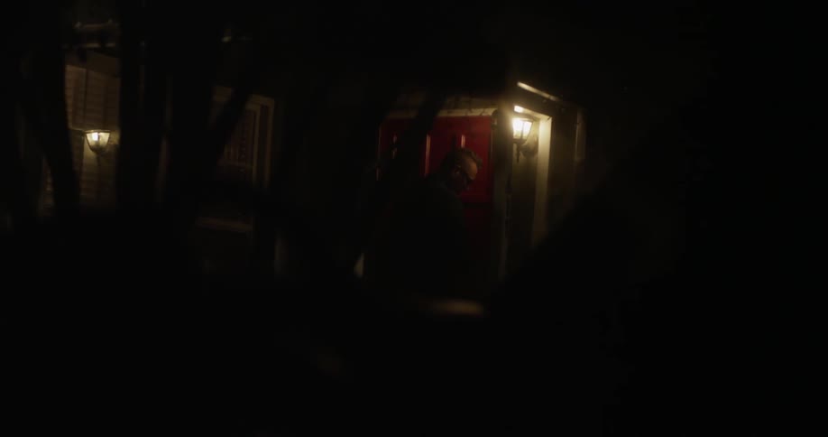 Man walking through the red door of his house to come outside at night