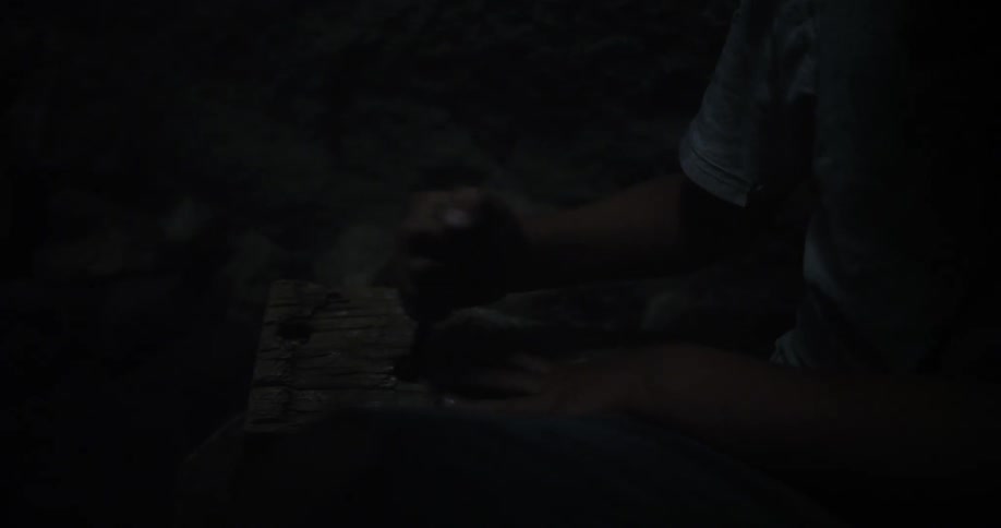 A person stabs a piece of wood with a large nail in the dark