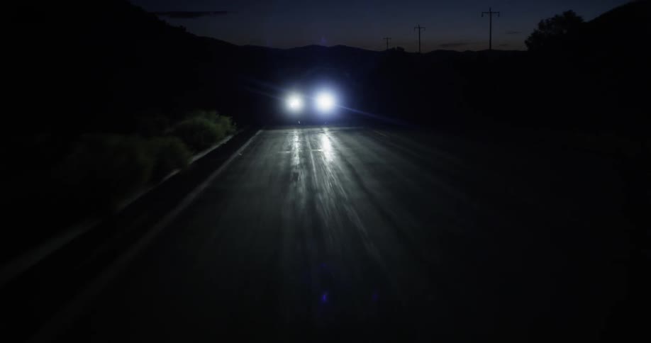 Headlights of a vehicle as it travels along a dark road