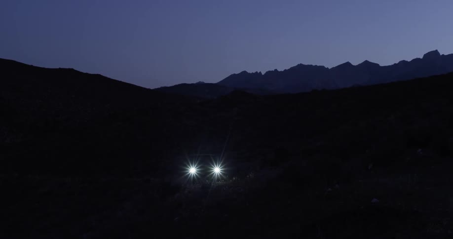 A car's headlights can be seen driving forward in a dark area