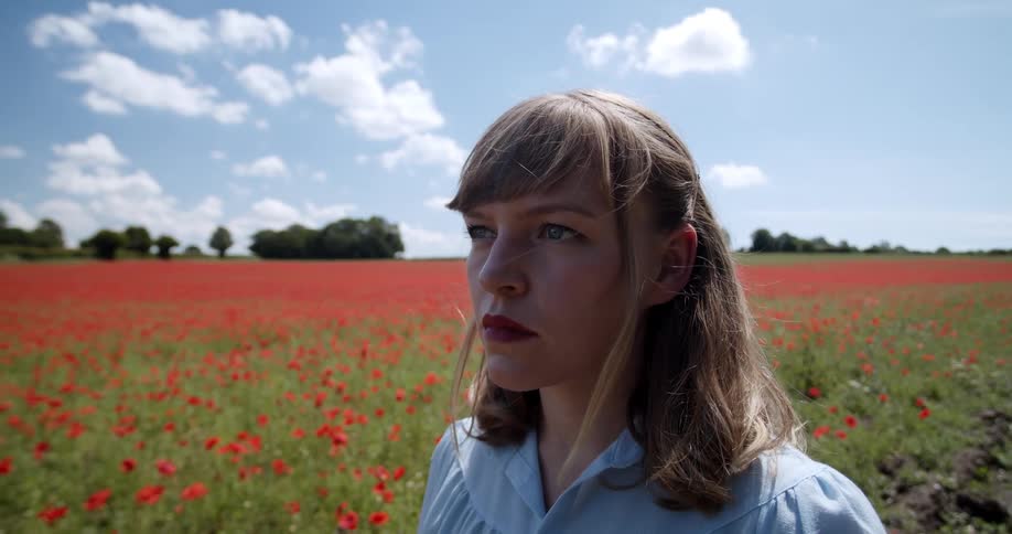 Blonde woman walks on a dirt road along a prairie with red wild flowers