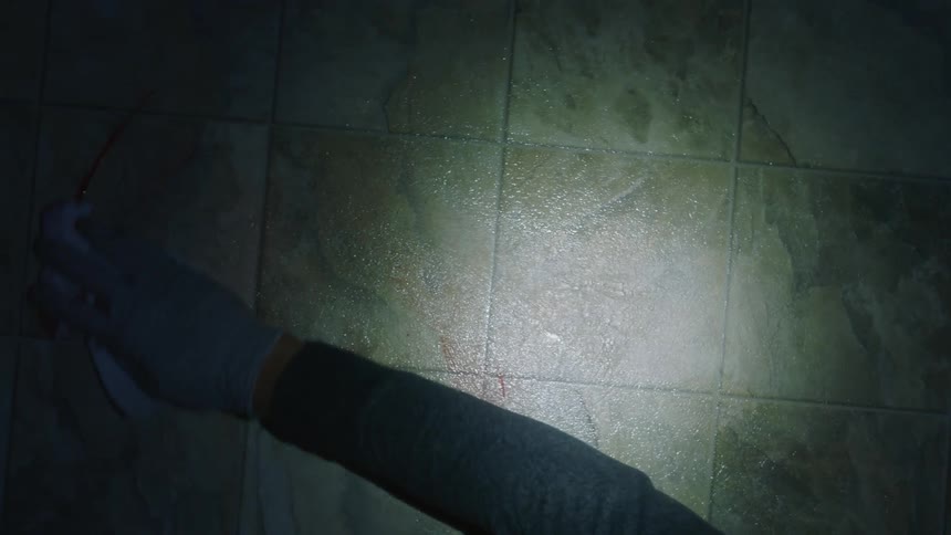 A gloved hand cleans blood off linoleum flooring with a rag