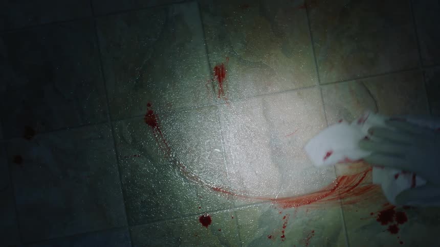 White gloved hand wipes up blood from a tiled floor with a cloth