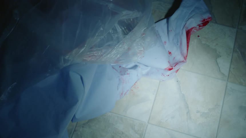 A bloody shirt lies on a linoleum floor in the dark