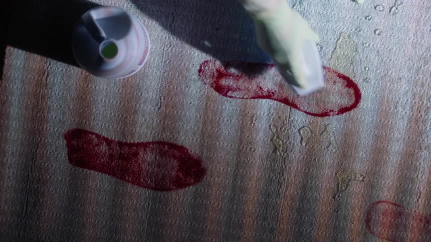 A person wearing kitchen gloves cleans bloody footprints with a brush