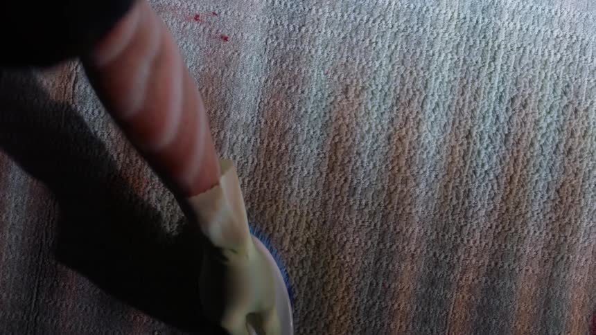 A person wearing kitchen gloves is cleaning blood stains from a rug with a brush