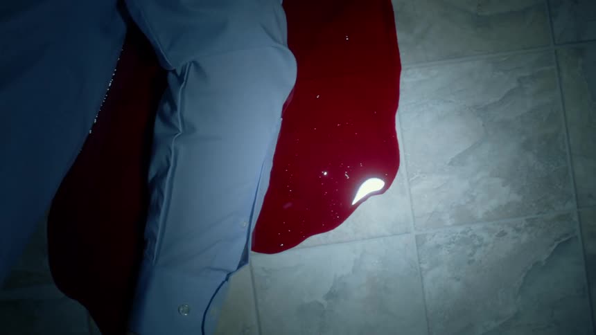A dead body lies in a pool of blood on a linoleum floor