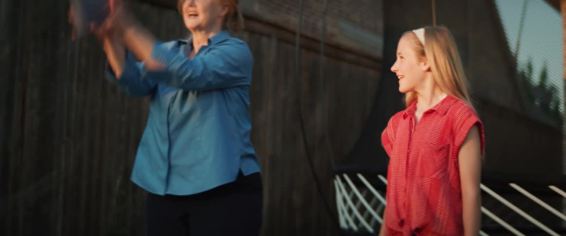Woman tosses a beanbag and laughs as a young girl stands next to her smiling