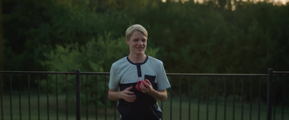 Two boys play bean bag toss beside a fence and building