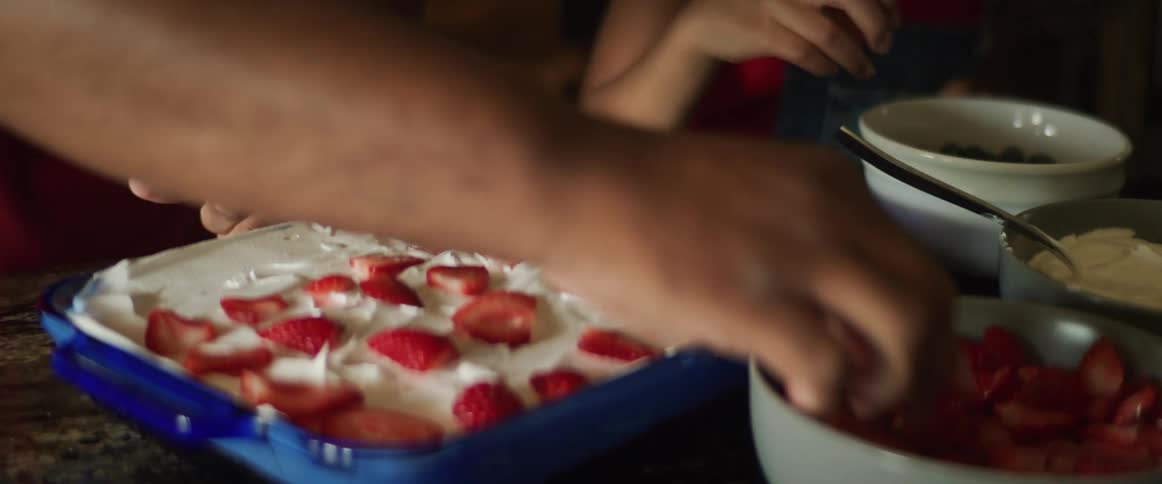 A father and child putting fruit on a dessert in a blue casserole dish