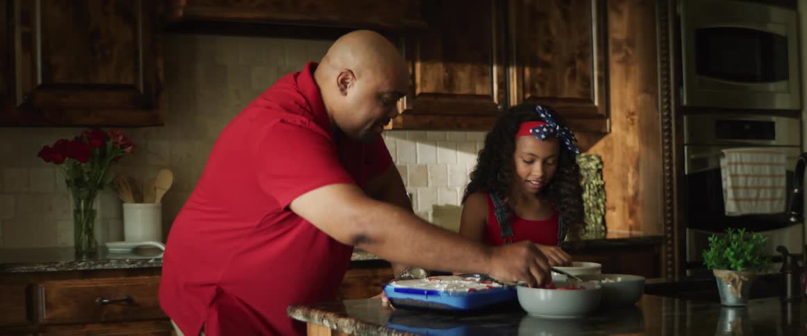 Father and daughter laugh as they decorate a cake