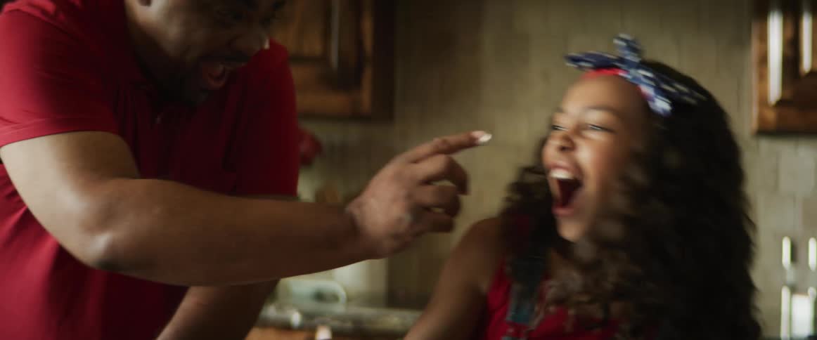 A father and daughter smear icing on each others face as they prepare dessert together in a kitchen