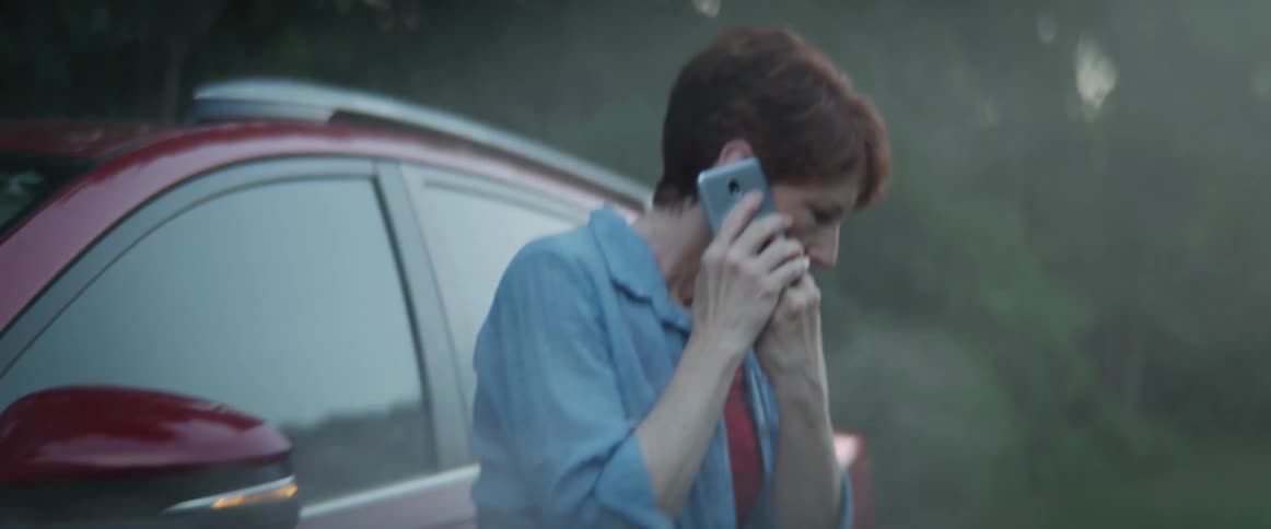 A woman exits her smoking vehicle and talks with agitation on her smartphone