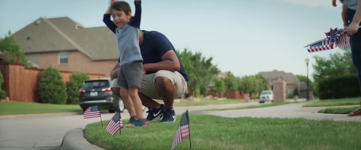 A young boy places a small flag in the neighborhood grass surrounded by his parents and baby sister