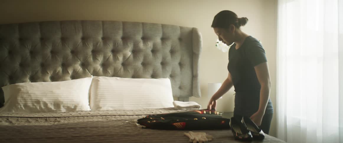 An Asian woman lays her military uniform on a bed, preparing it for use.