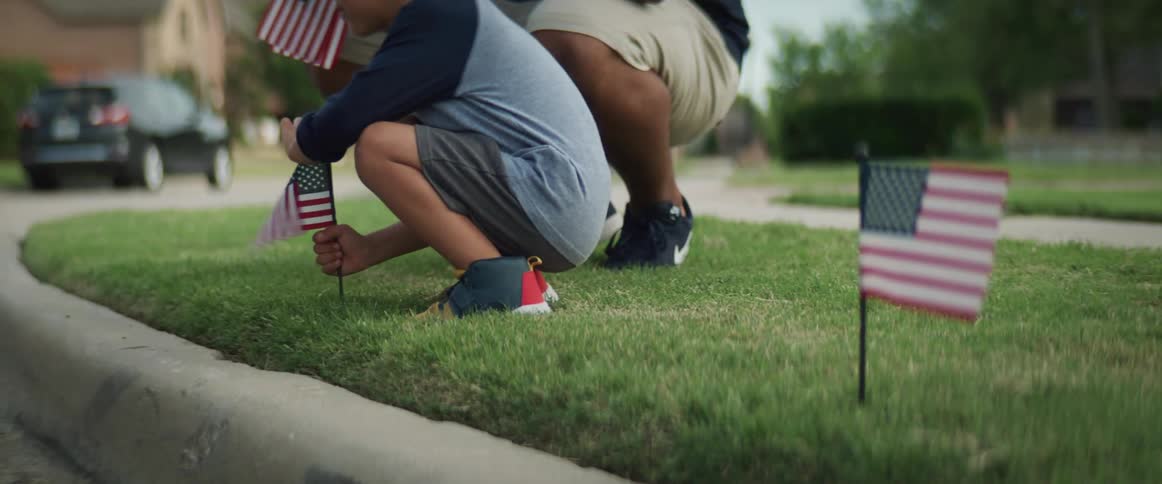 A dad helps his son put little american flags in the grass