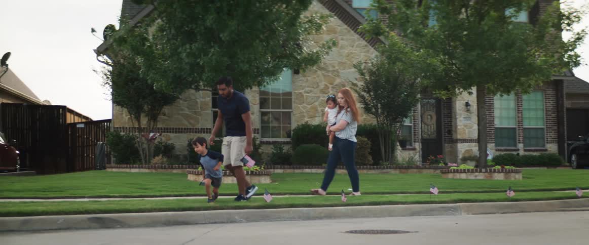 Parents and their two small children place flags into the grass along the sidewalk in front of a home