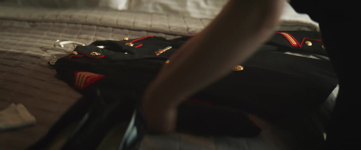 An Asian woman places her military uniform on a bed and polishes the buttons
