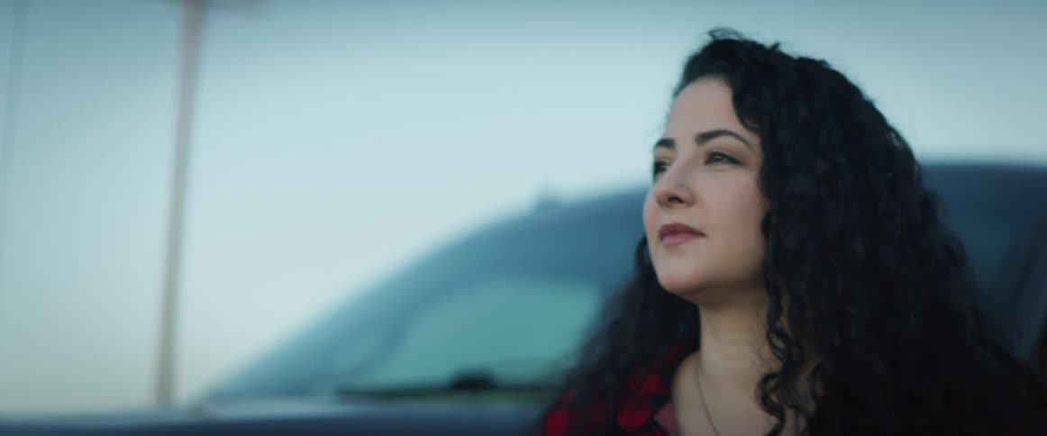 Woman with a dark curly hair and a red striped shirt gets out of a black pickup trucks smiles and looks around