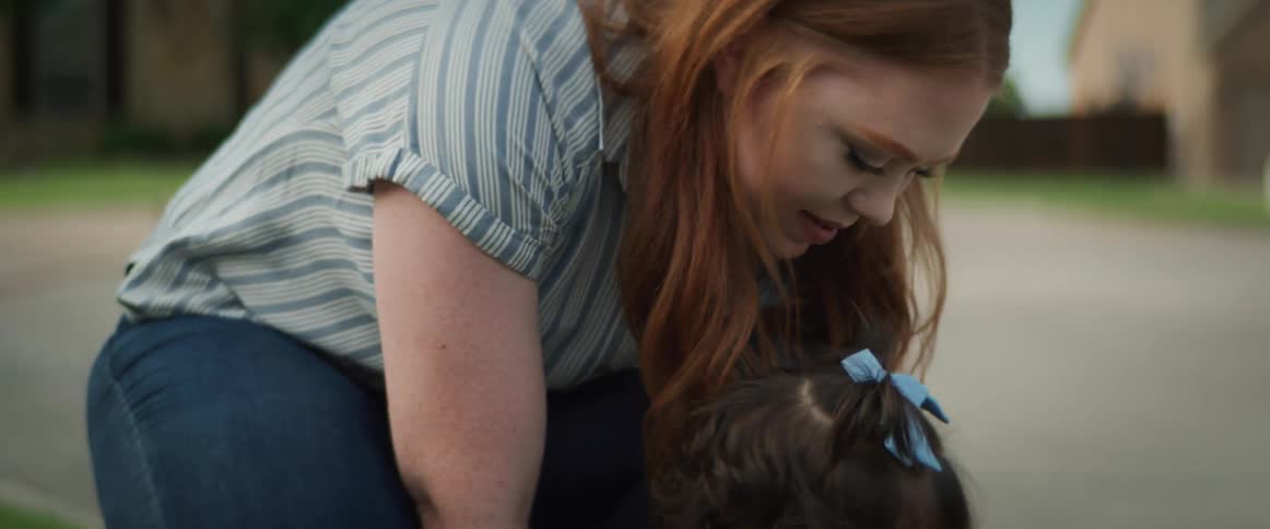 A woman bends down to a toddler girl placing a flag into the grass
