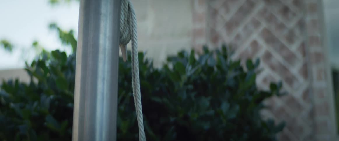 Man wraps rope at bottom of flagpole standing near house window