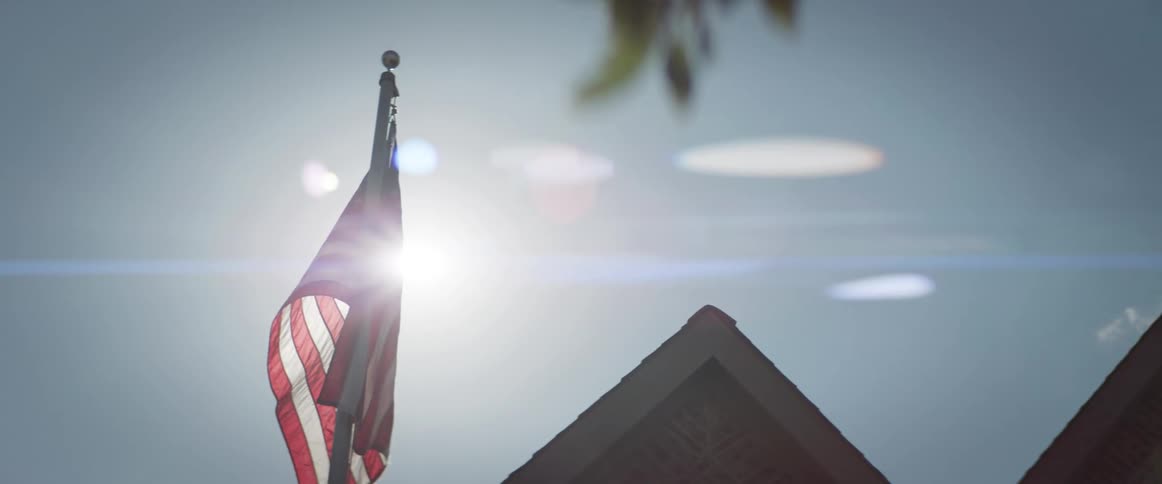 The american flag attached to a pole flutters in the wind under the sun