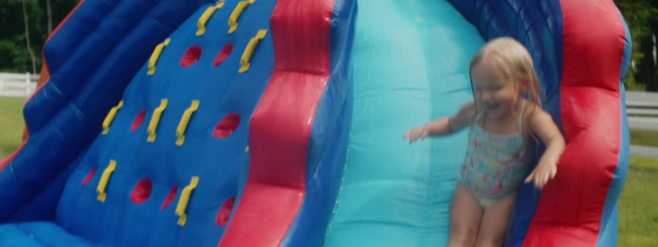 Little girl slides down an inflatable playground in the backyard