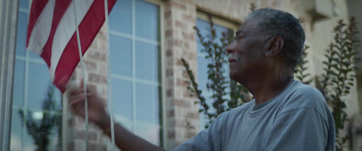 Elderly man raises an american flag on a flagpole outside a building