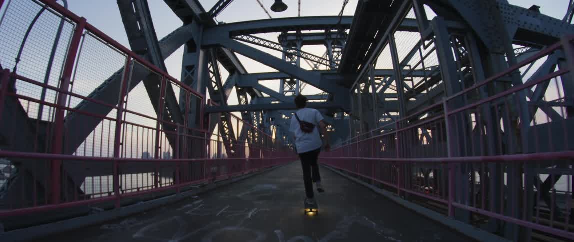 A teenage boy riding a skateboard over a city bridge