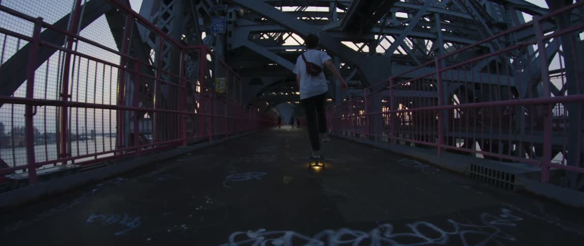 Skateboarder crosses bridge over water across from city skyline